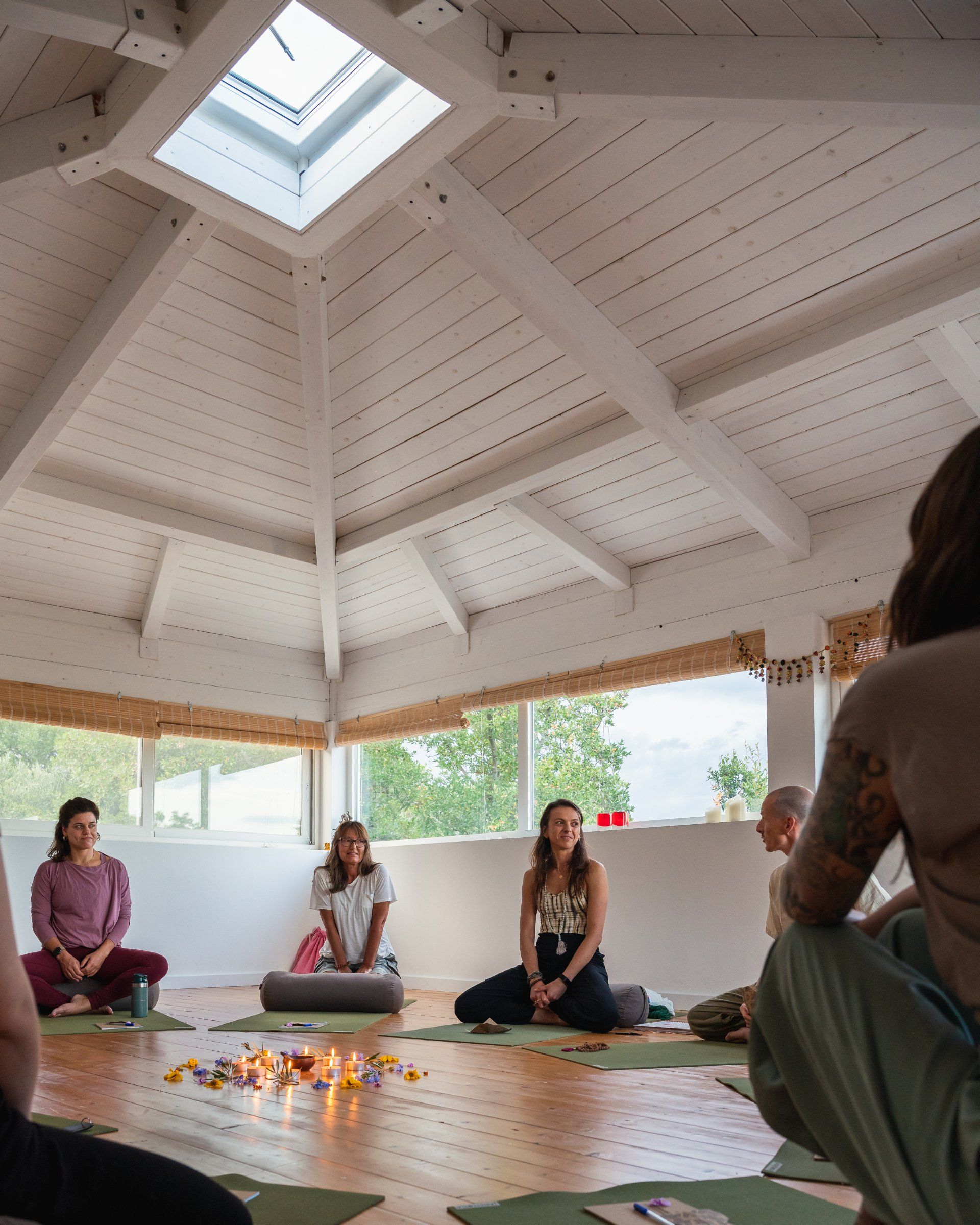People meditating in a white, octagonal room with a skylight. Lit candles on the floor.
