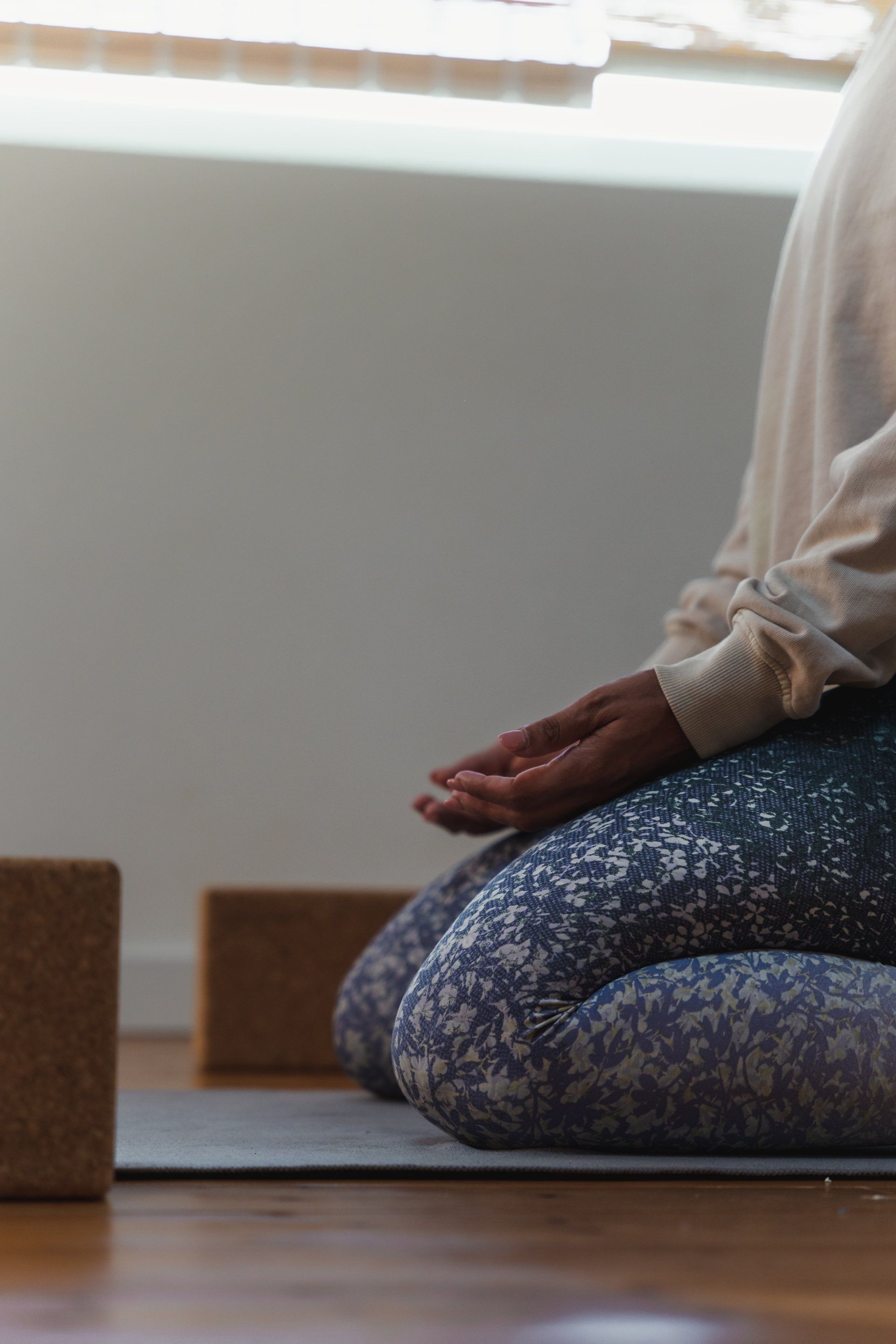 Person in seated meditation pose on a mat; hands in lap, legs crossed, near wooden blocks.