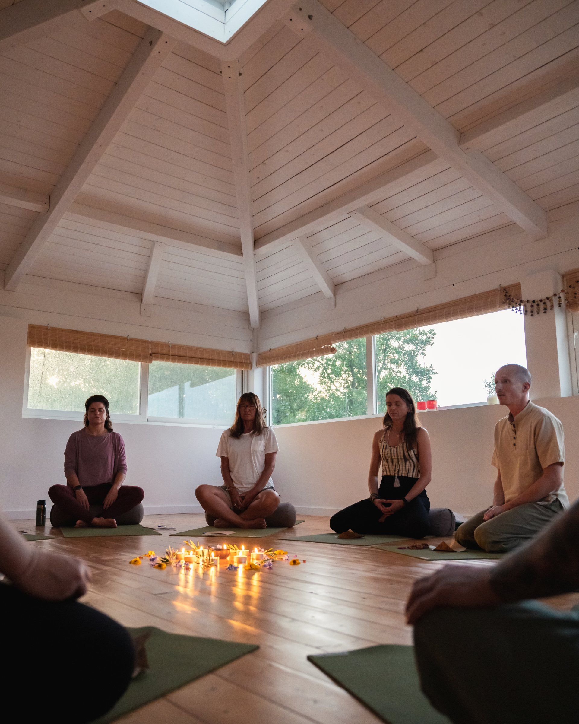 People meditate in a white-ceilinged room with candles. The natural light fills the space.
