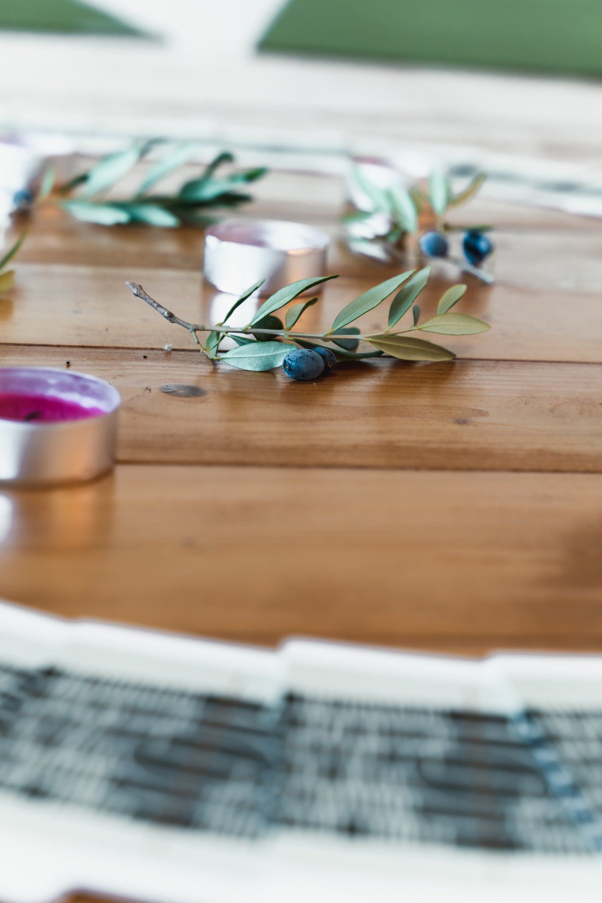 Close-up of a wooden surface with olive branches, berries, and small candles.