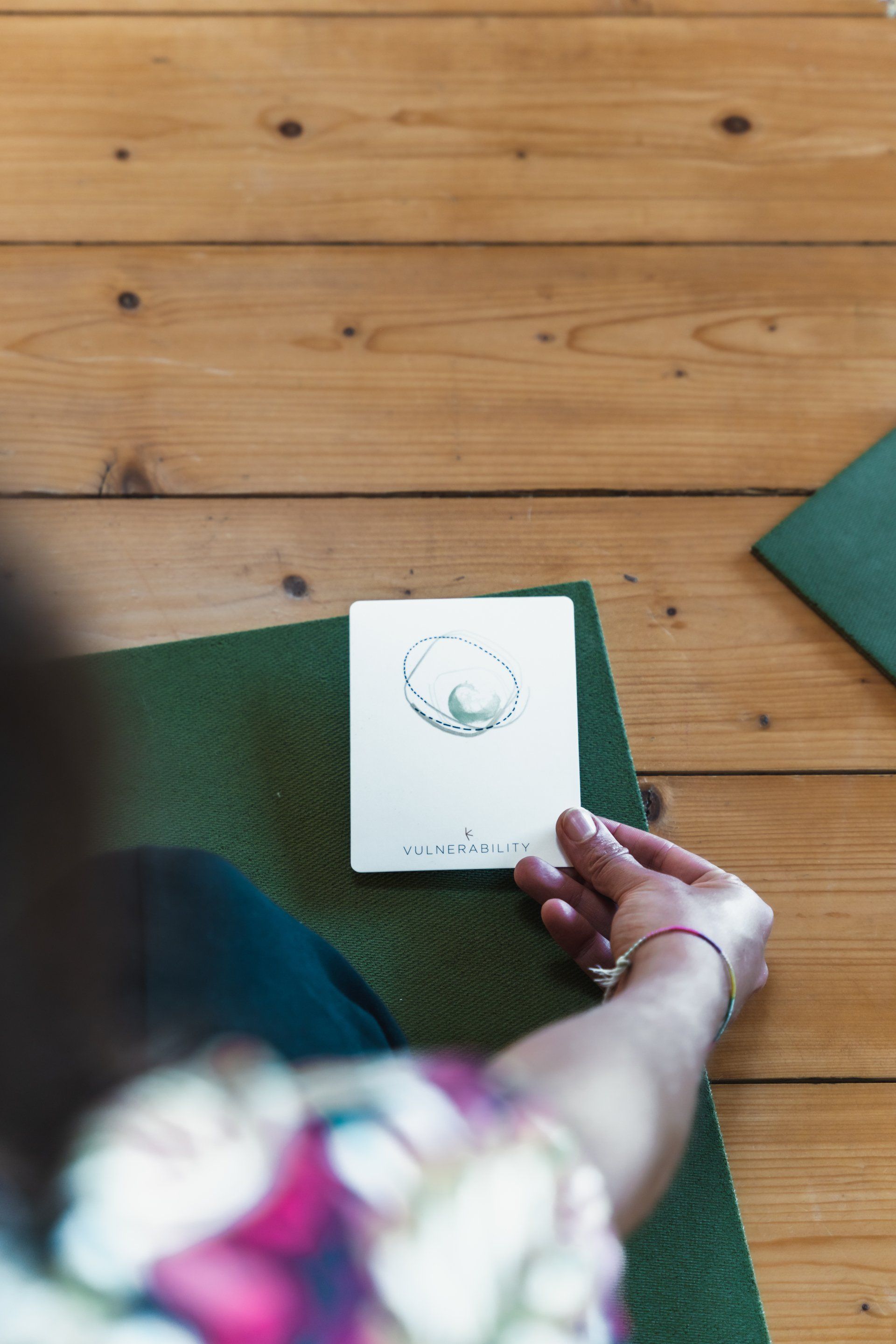 Hand holding a white card with an abstract design on a green mat, wooden floor in background.