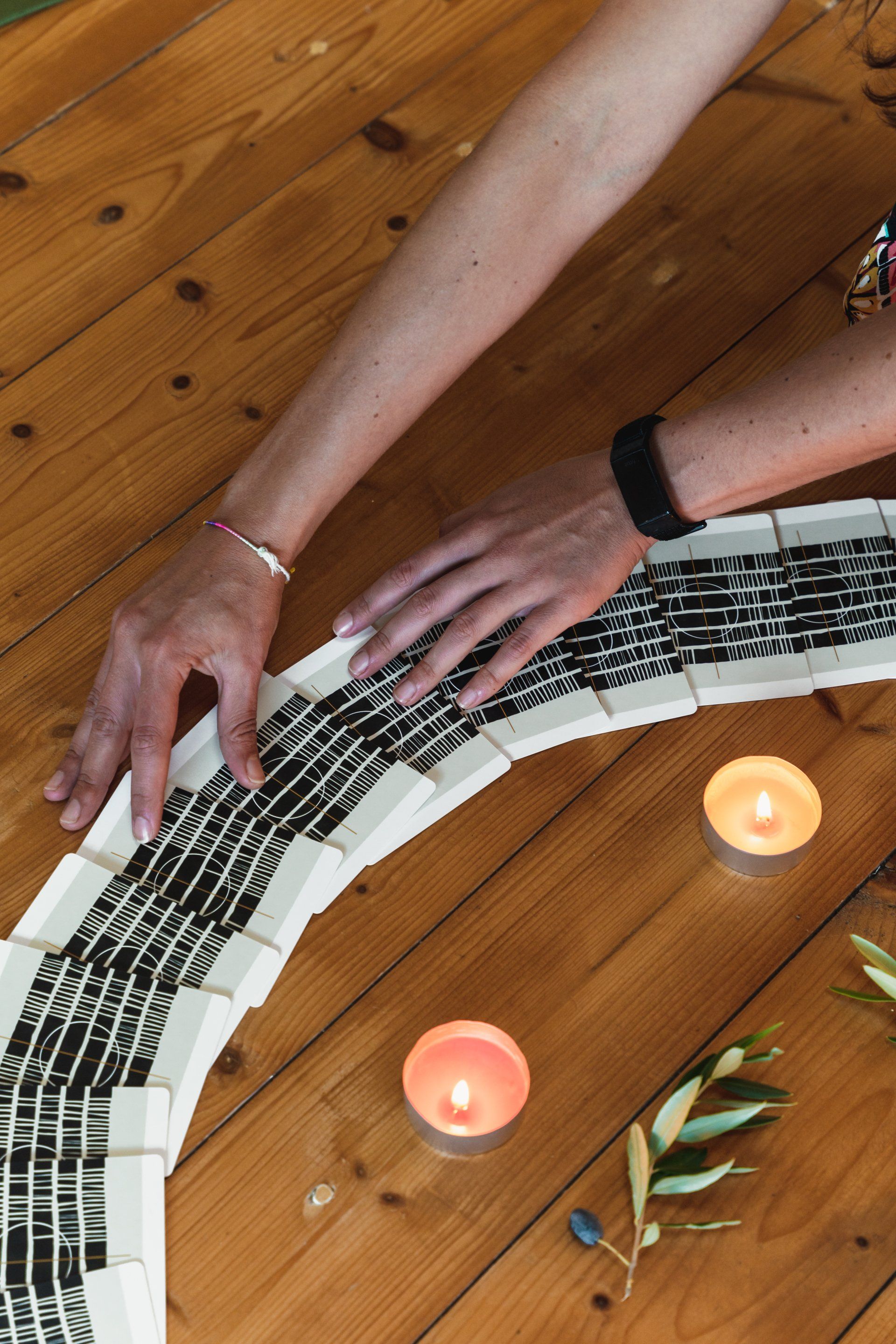 Hands arranging a woven black and white piece on wooden floor, lit by candles and greenery.