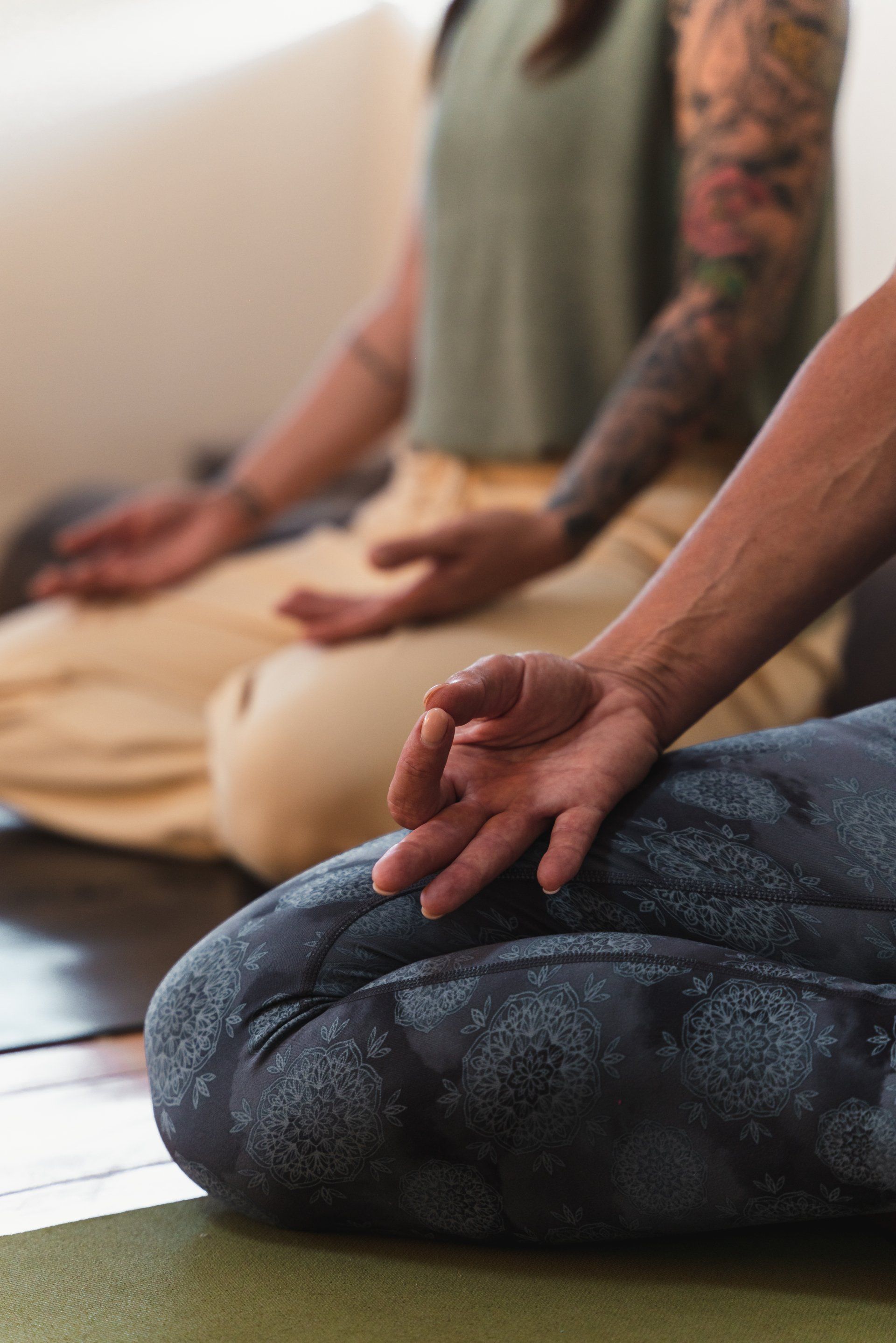 Hands in mudra position; person seated, legs crossed, wearing blue leggings, meditating.
