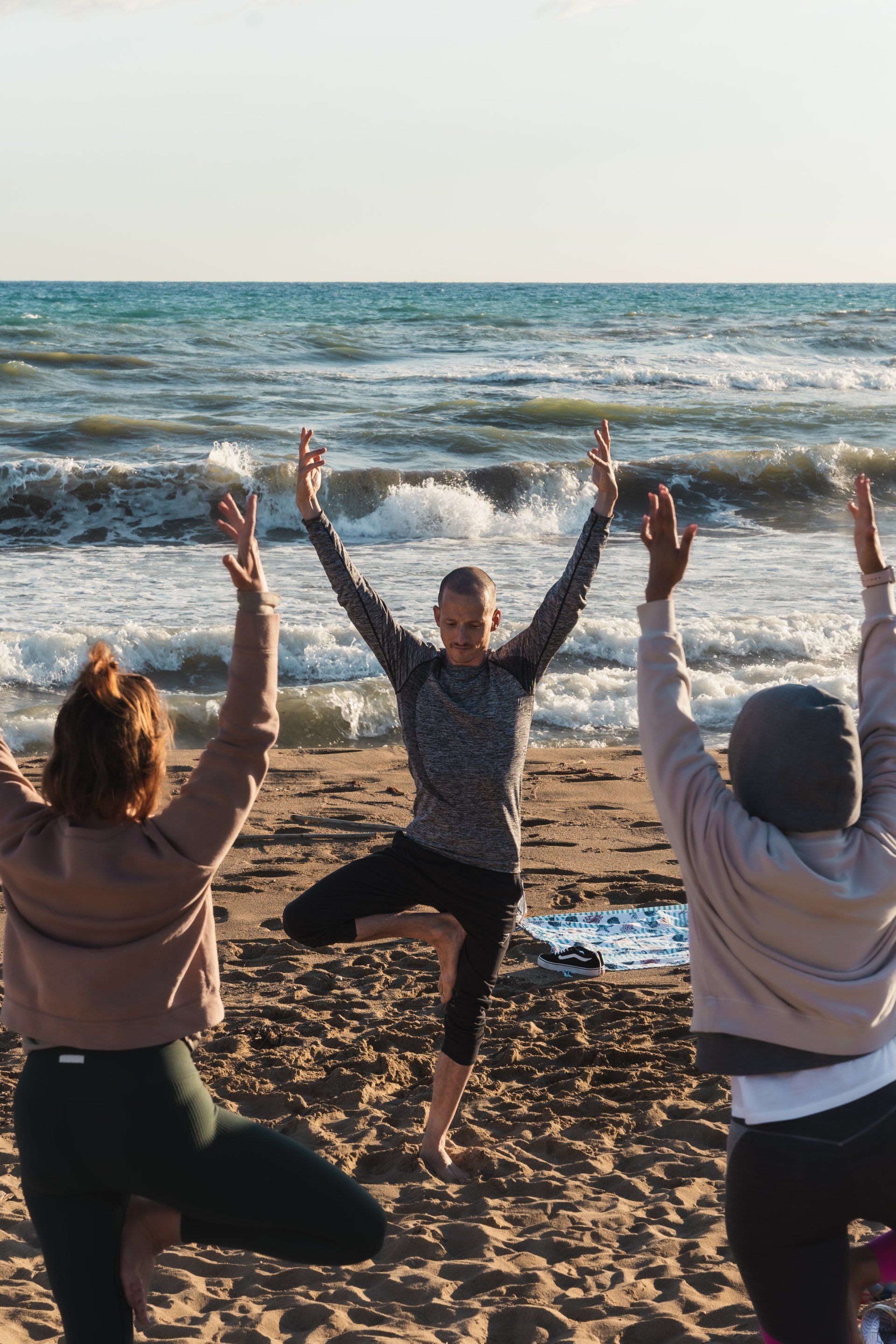 People doing yoga on a beach with the ocean in the background, arms raised in the air.