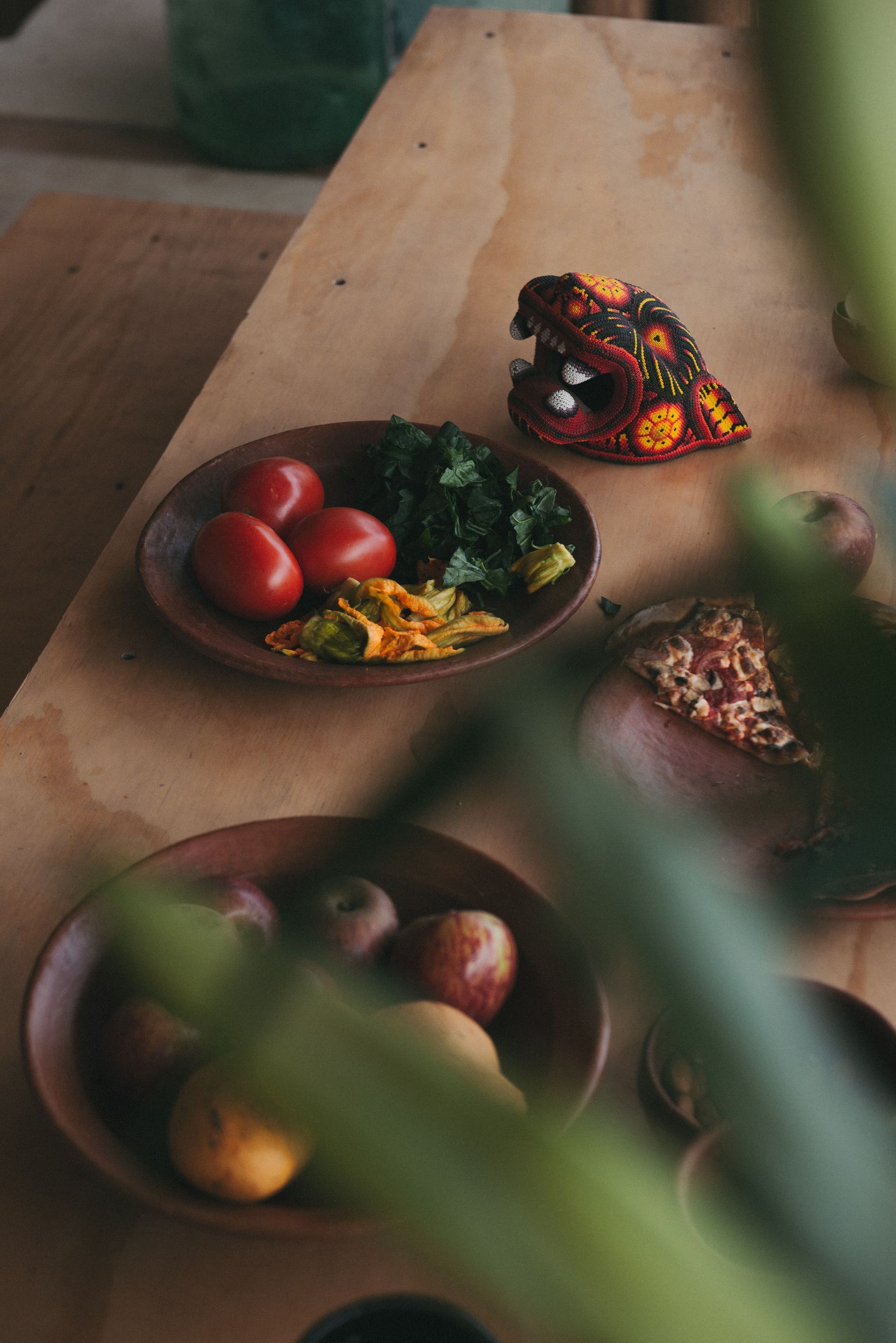 Wooden table with bowls of tomatoes, greens, fruits, and a decorative dragon head.