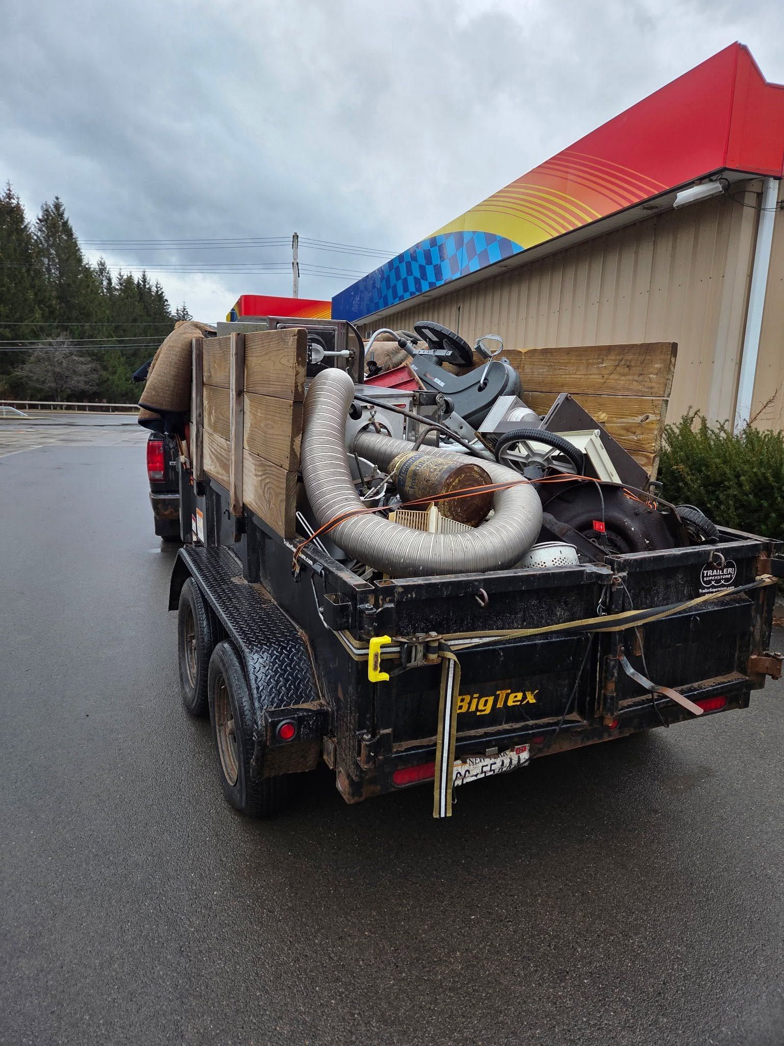 Truck loaded with scrap metal on a wet roadside beside a colorful building