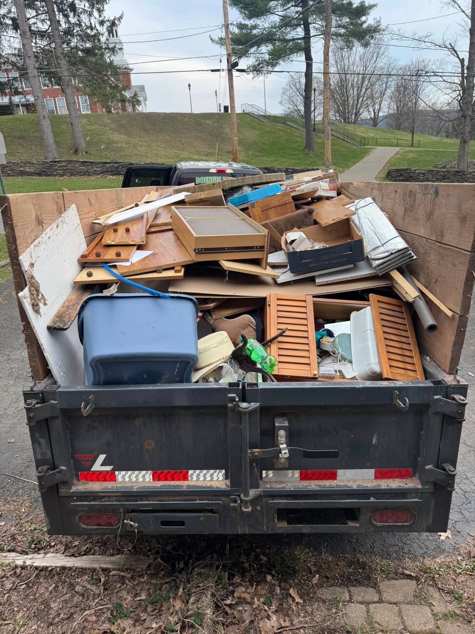 Red dumpster overflowing with trash in a wooded area; debris scattered around the base.