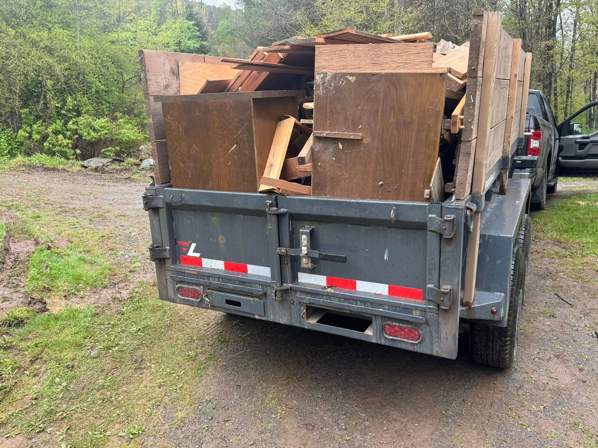 Red dumpster overflowing with trash in a wooded area; debris scattered around the base.