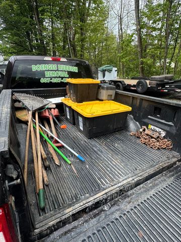 Pickup truck bed with tools, buckets, and branches in a wooded outdoor setting