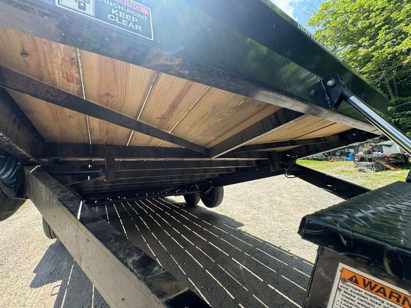Underside of a black trailer with wooden floor panels, viewed from below in a gravel lot.