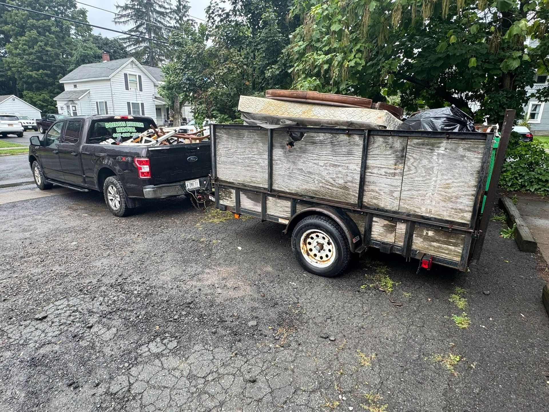 Dark pickup truck towing a trailer loaded with debris on a wet, paved surface.