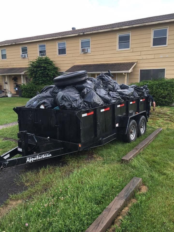 A black trailer filled with black trash bags and a tire, parked in front of a building on grass.