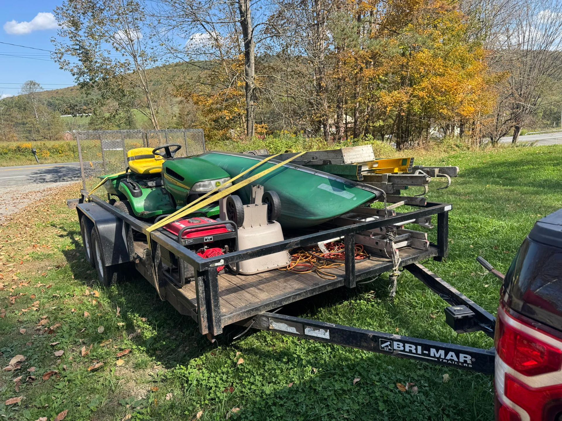 A utility trailer loaded with lawn equipment, secured with straps, parked on grass.