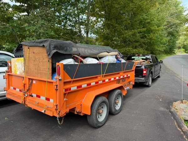 Orange trailer loaded with items, hitched to a black pickup truck on a paved road.