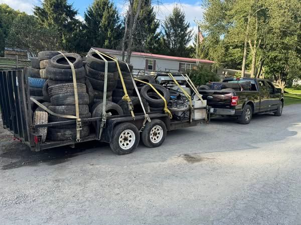 A pickup truck towing a trailer overflowing with used tires on a paved road.