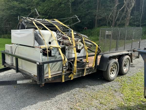 Trailer loaded with scrap metal and appliances, secured with yellow straps, outdoors.