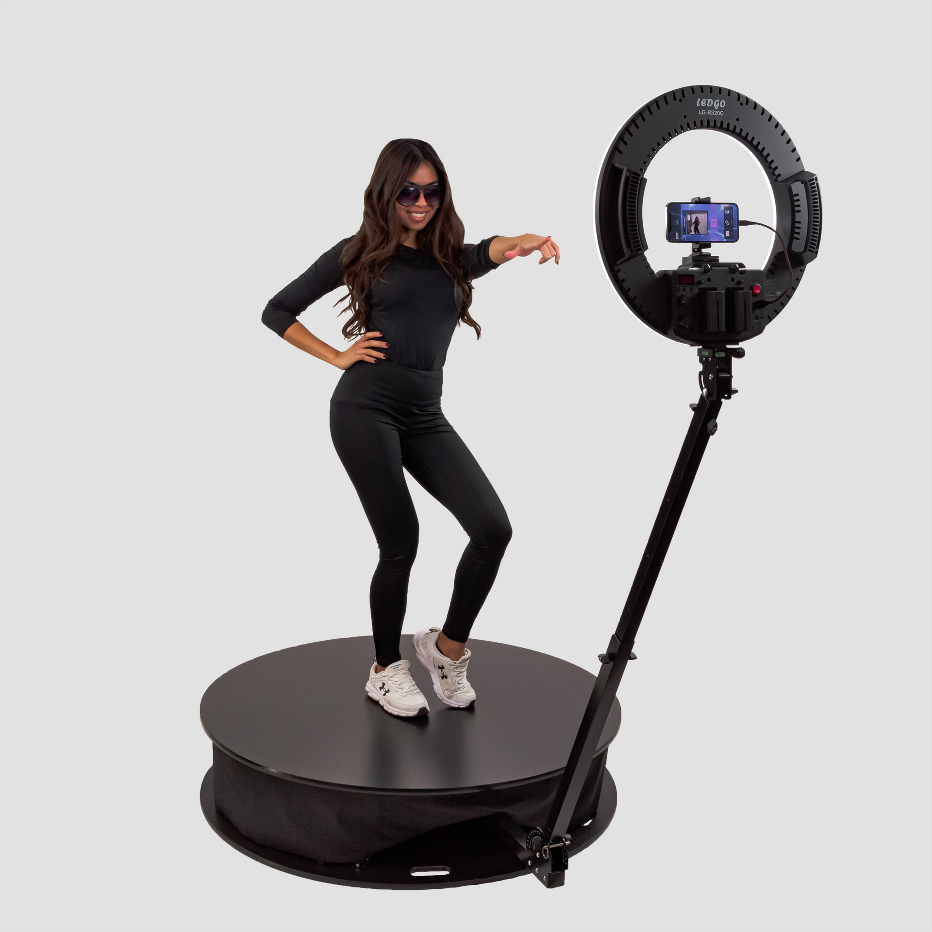 A woman is standing on a turntable next to a ring light.