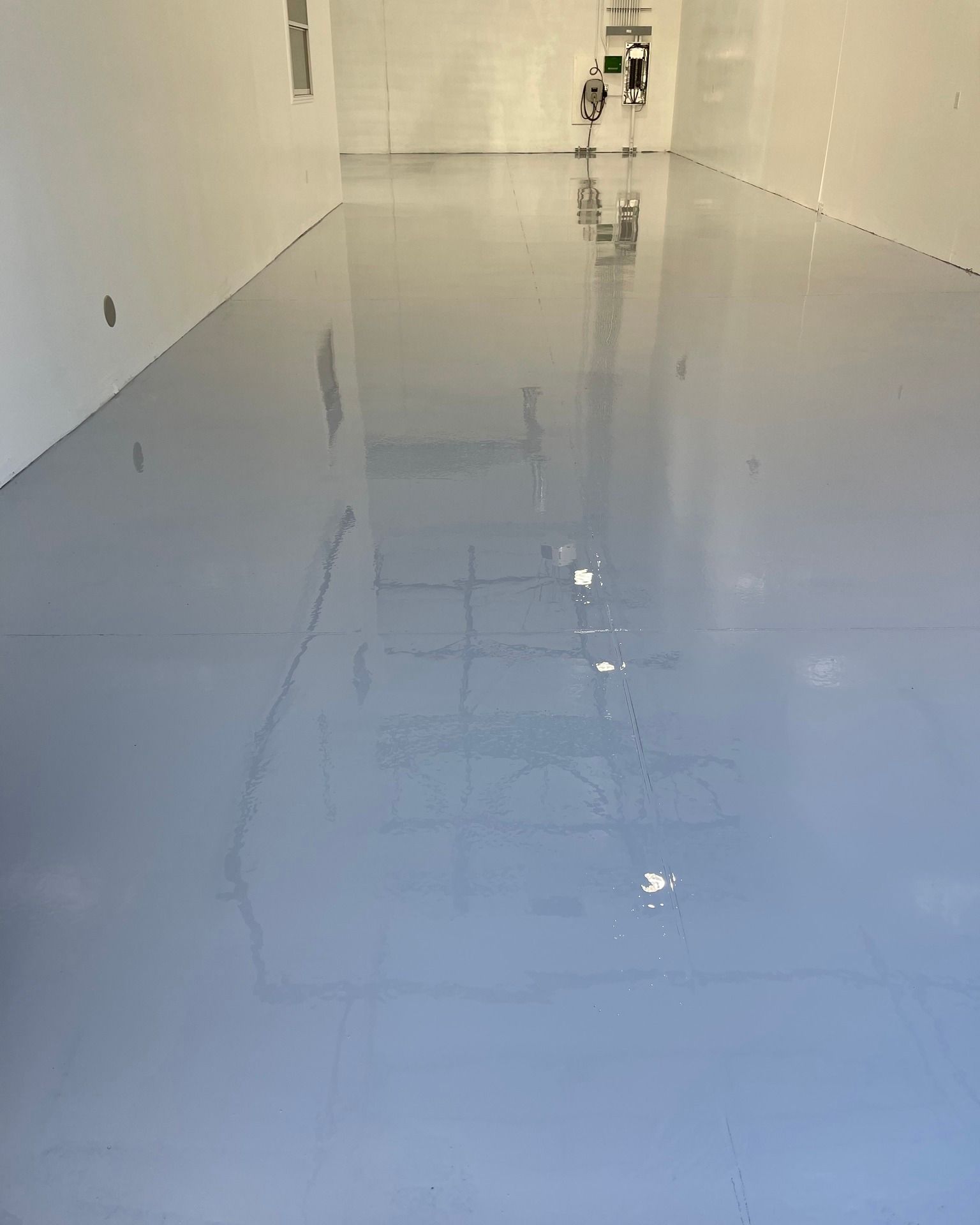 Glossy blue epoxy floor in a narrow white hallway with reflections and a door at the far end