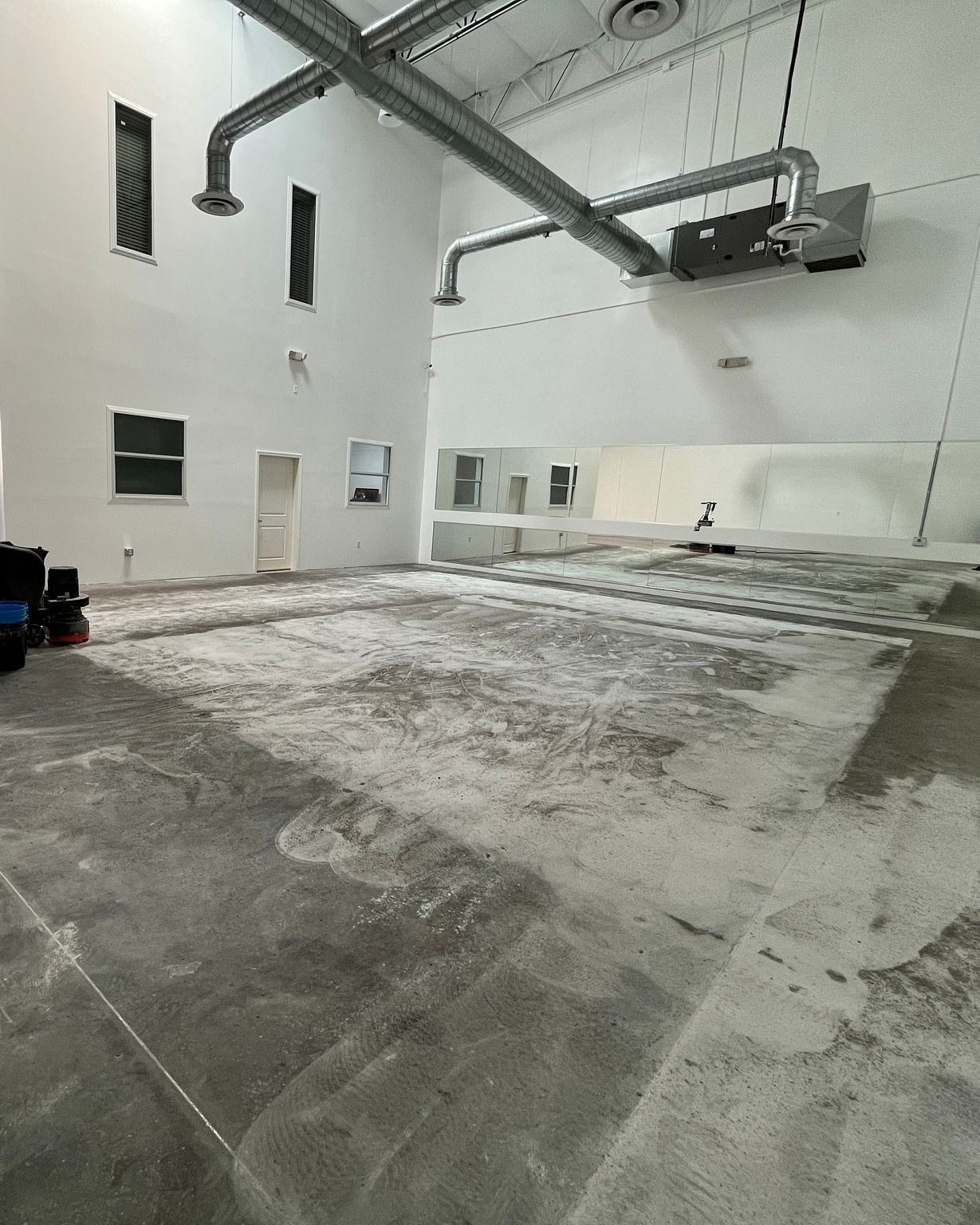 Large empty warehouse with concrete floors, white walls, exposed ceiling pipes, and a mounted projector.