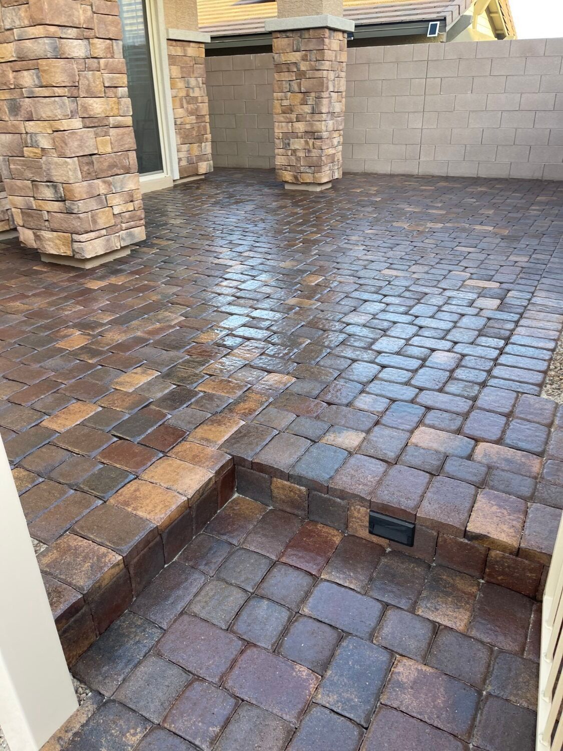 Stone paver patio with a small step down to a lower brick area beside stone columns and a wall