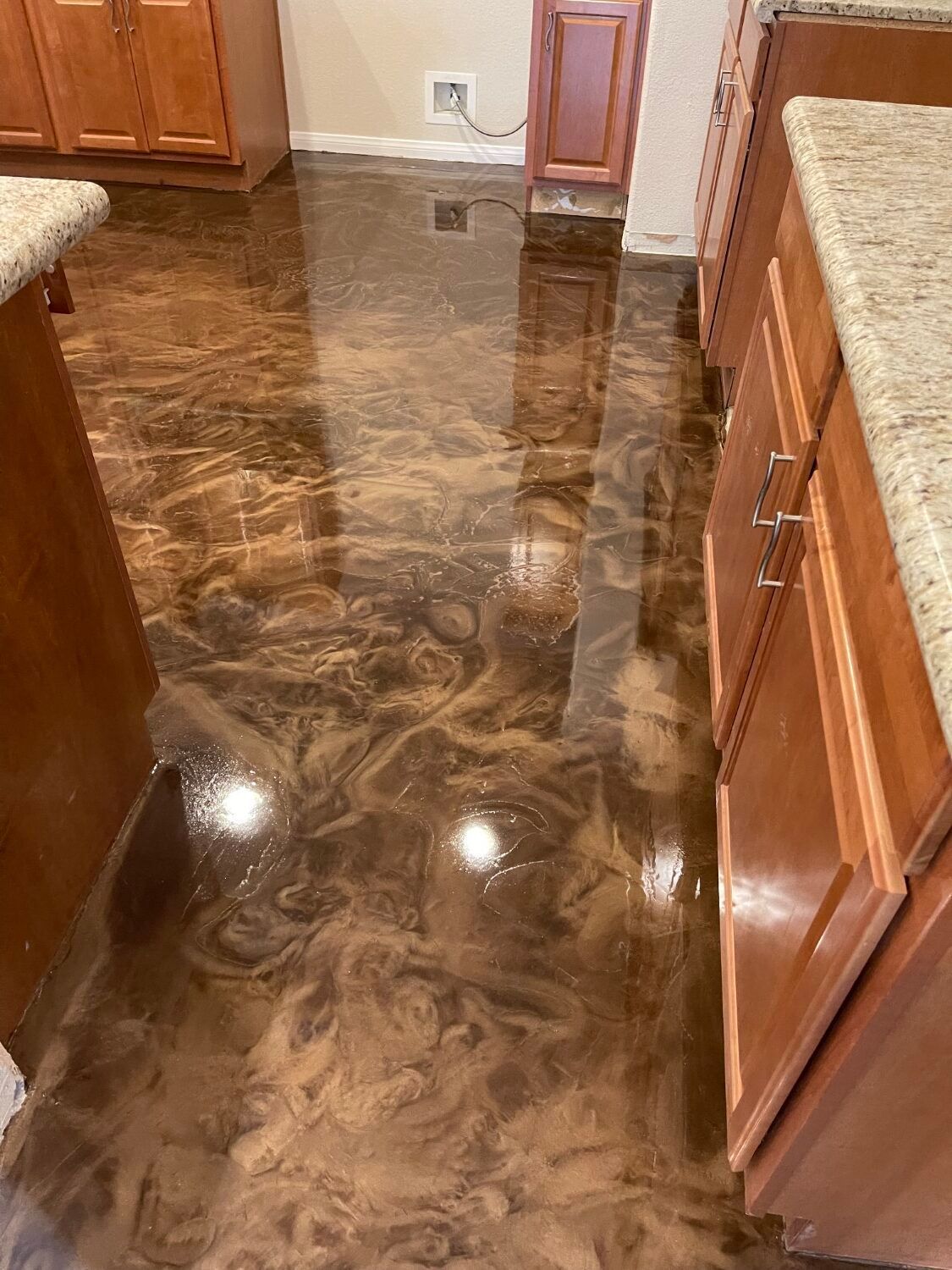 Polished brown marbled kitchen floor with reflective finish between wooden cabinets and counters