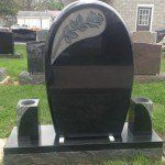 A black gravestone with a floral design on it is in a cemetery.