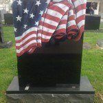 A black gravestone with an american flag on it in a cemetery.