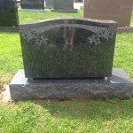 A black gravestone with flowers on it is sitting in the grass in a cemetery.