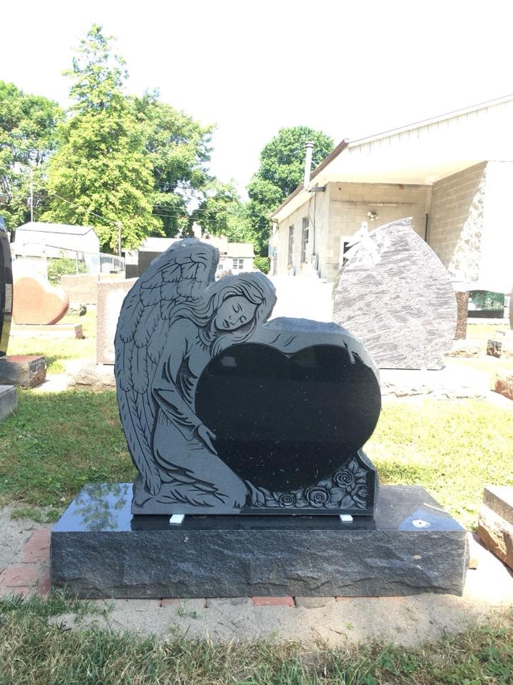 A black gravestone with an angel holding a heart in a cemetery.