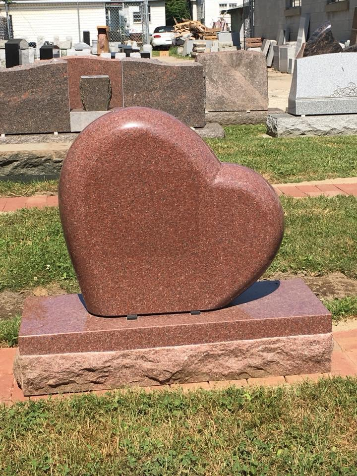 A gravestone in the shape of a heart is in a cemetery.