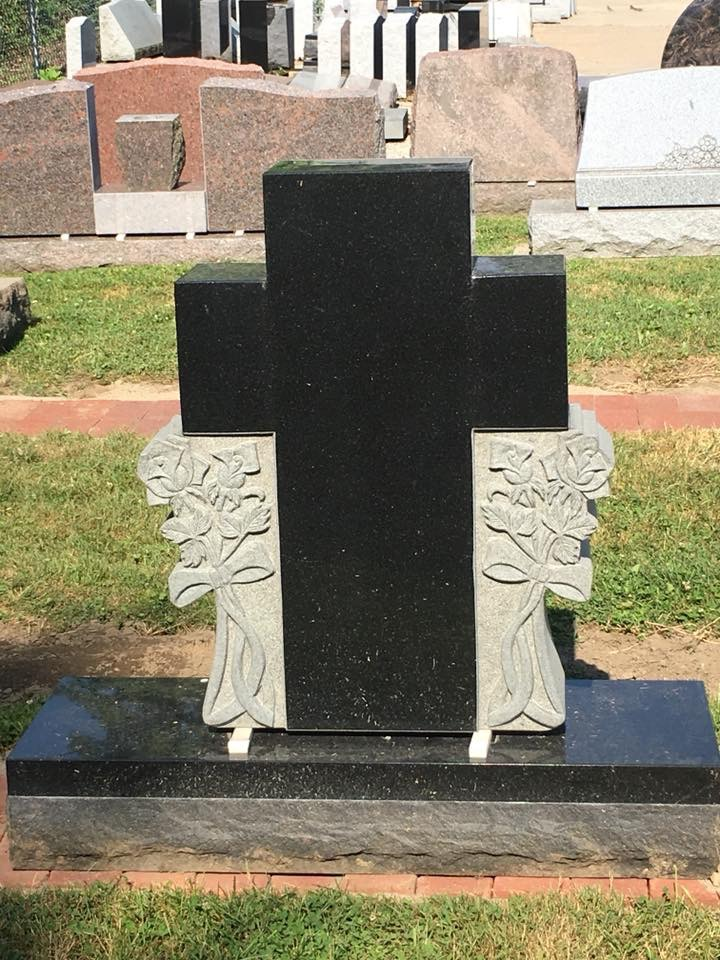A black gravestone with a cross on it in a cemetery