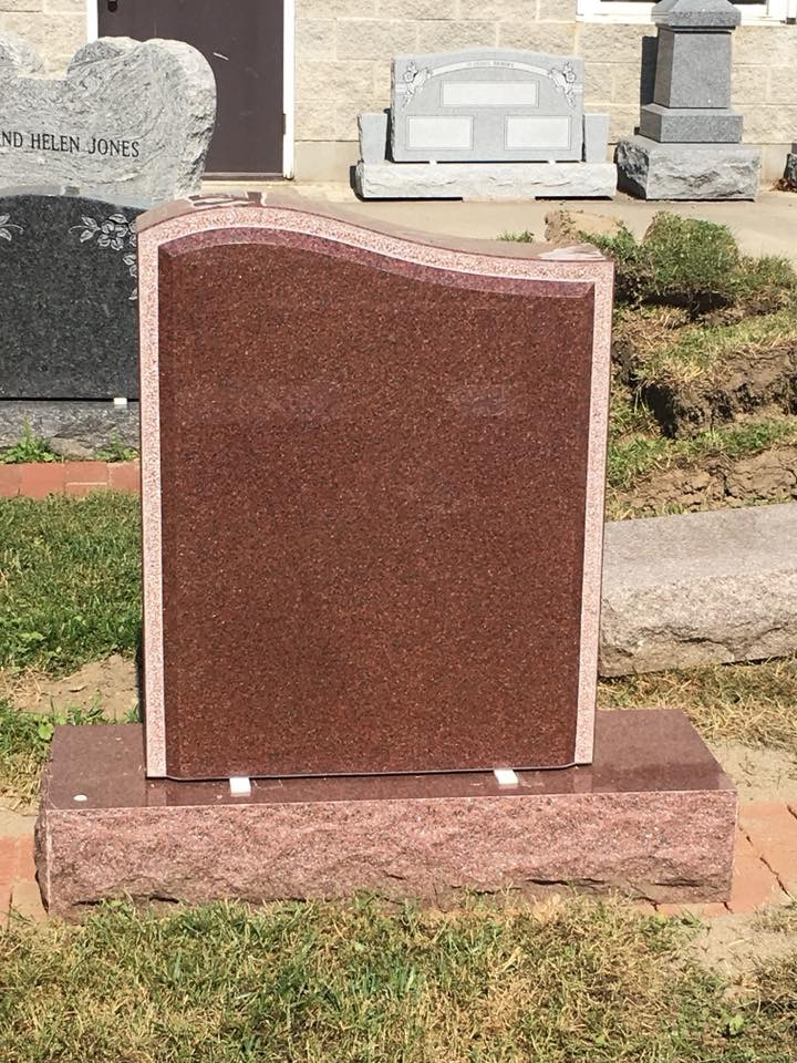 A red gravestone is sitting in the grass in front of a building.