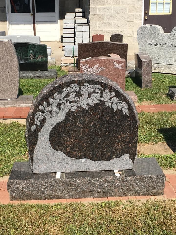 A gravestone with a tree carved into it is sitting in the grass.