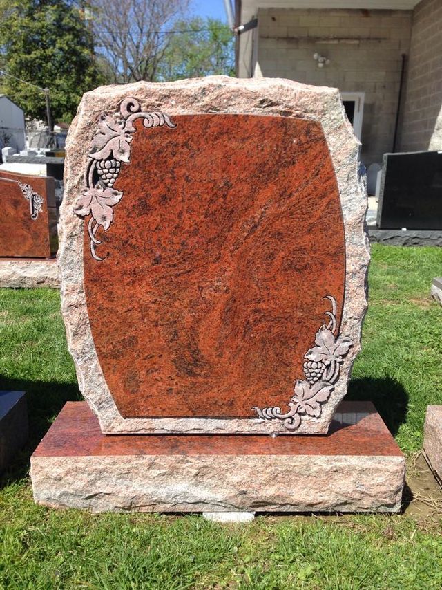 A red gravestone is sitting on top of a grass covered field.