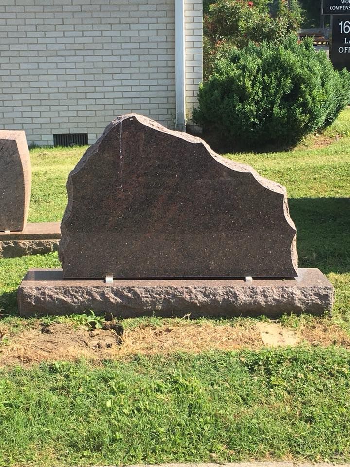A large rock is sitting in the grass in front of a brick building.