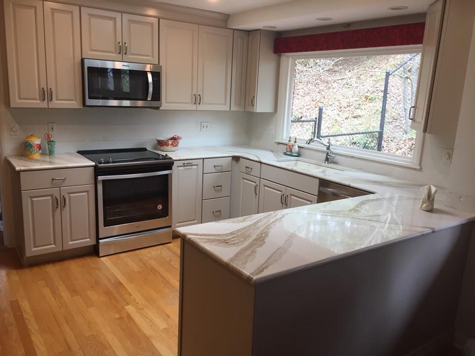 A kitchen with white cabinets , stainless steel appliances , a sink , and a window.