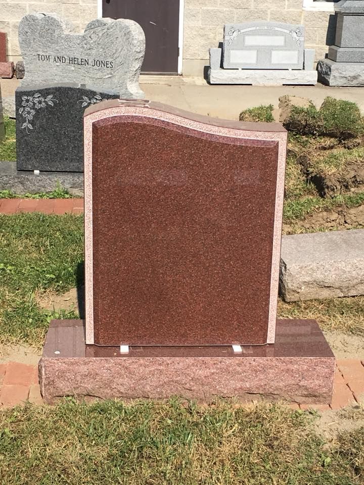 A red gravestone is sitting in the grass in front of a building.
