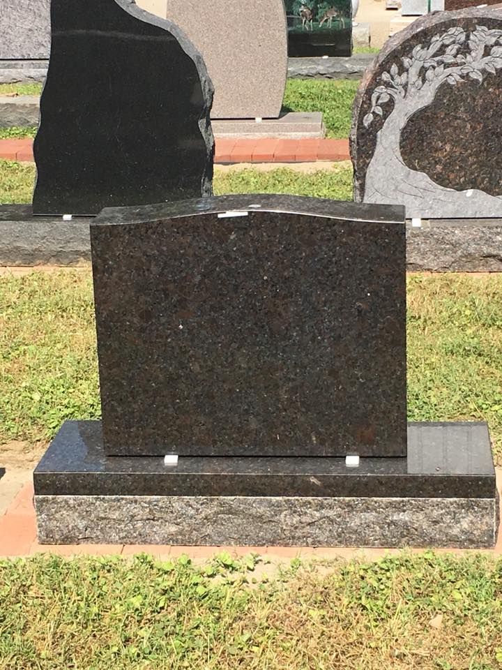 A black gravestone is sitting in the grass in a cemetery.