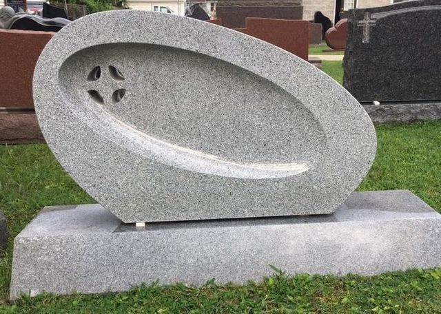 A gravestone with a cross carved into it is sitting in the grass.
