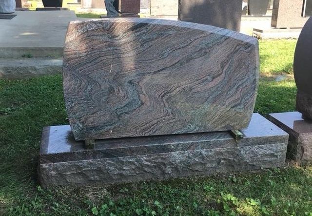 A gravestone is sitting in the grass in a cemetery.