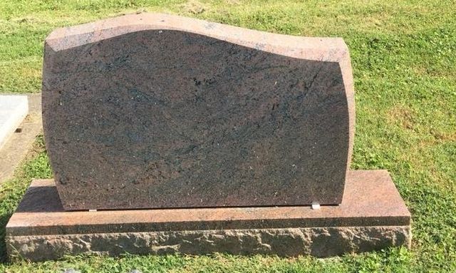 A gravestone is sitting in the grass in a cemetery.