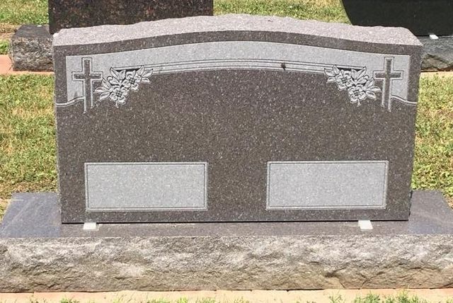 A gravestone with a cross on it is in a cemetery.