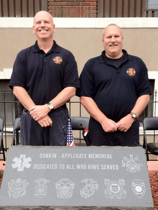 Two men are standing in front of a stone that says dunkin ' applegate memorial