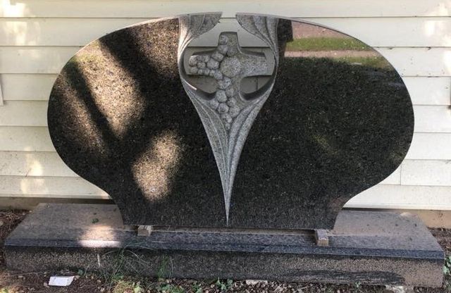 A black gravestone with a cross on it is sitting in front of a white house.