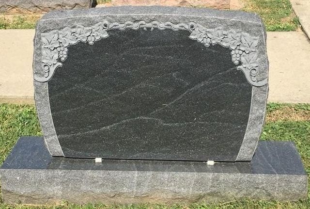 A black gravestone with a floral design on it is sitting in the grass.
