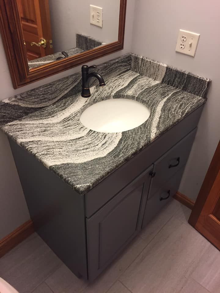 A bathroom sink with a granite counter top and a mirror.