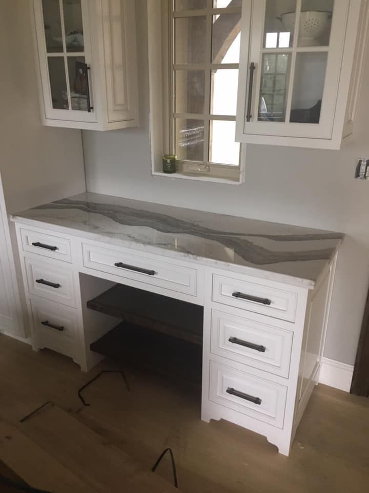 A white desk with drawers and a marble counter top in a kitchen.