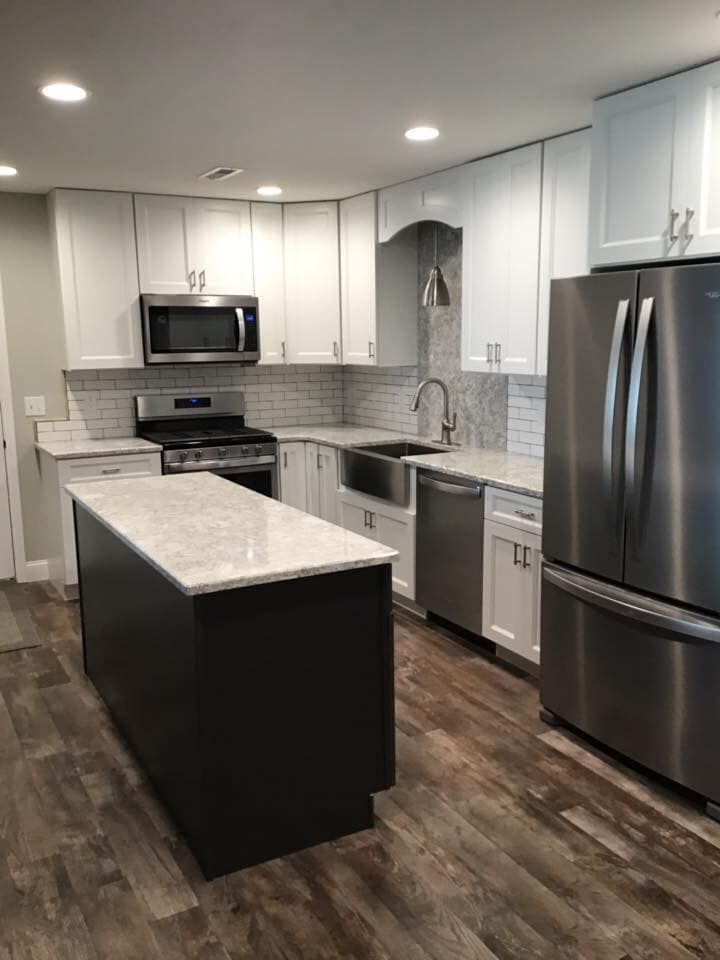 A kitchen with white cabinets , stainless steel appliances , a sink , and a large island.