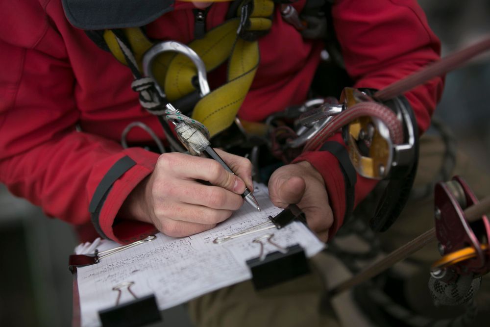 Person in Red Jacket and Safety Harness Writing on a Notepad — Hunter Fire & Safety in Port Stephens, NSW