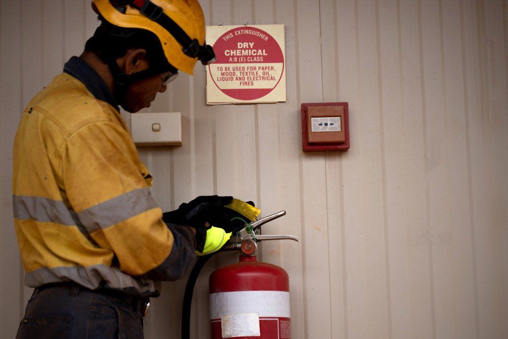 Person in Safety Gear Inspecting a Red Fire Extinguisher — Hunter Fire & Safety in Edgeworth, NSW